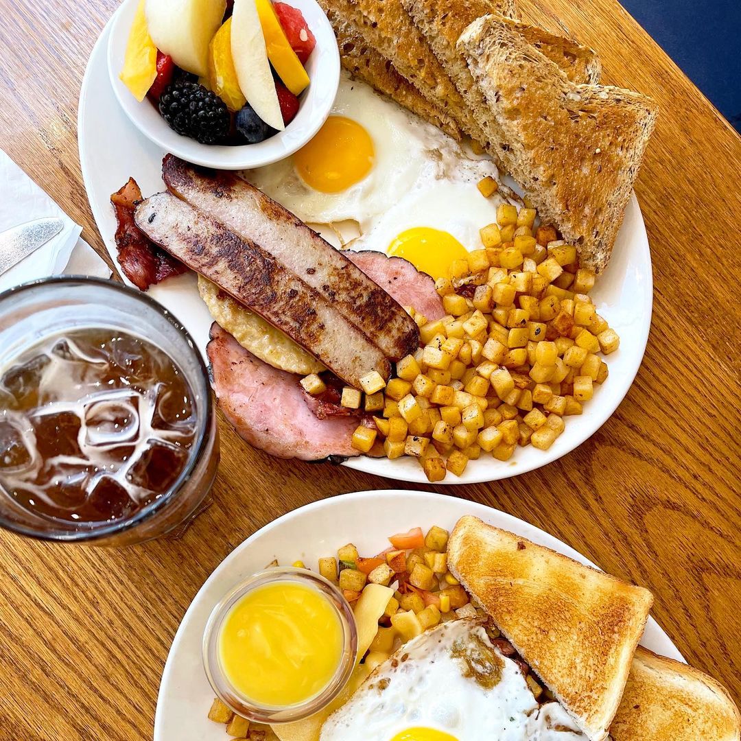 Assorted breakfast platters with fried eggs, toast, hasbrowns and sausages on a wooden table.