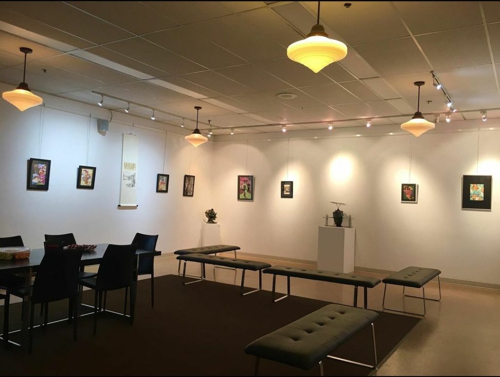 A dimly lit gallery filled with art work along the walls with seating areas all around.