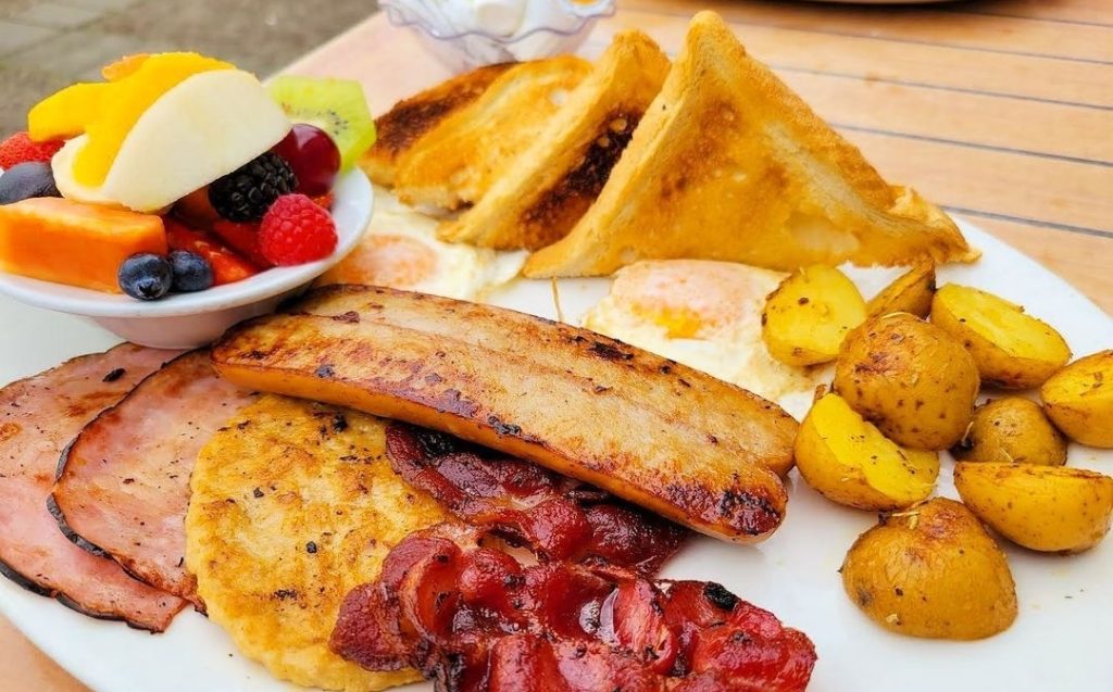 A big breakfast of bacon, egg, sausage, ham, potatoes, toast and fruit